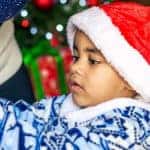 Young boy wearing a Santa hat helping to decorate a Christmas tree
