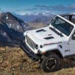 Jeep Wrangler top off driving off-road in front of mountains