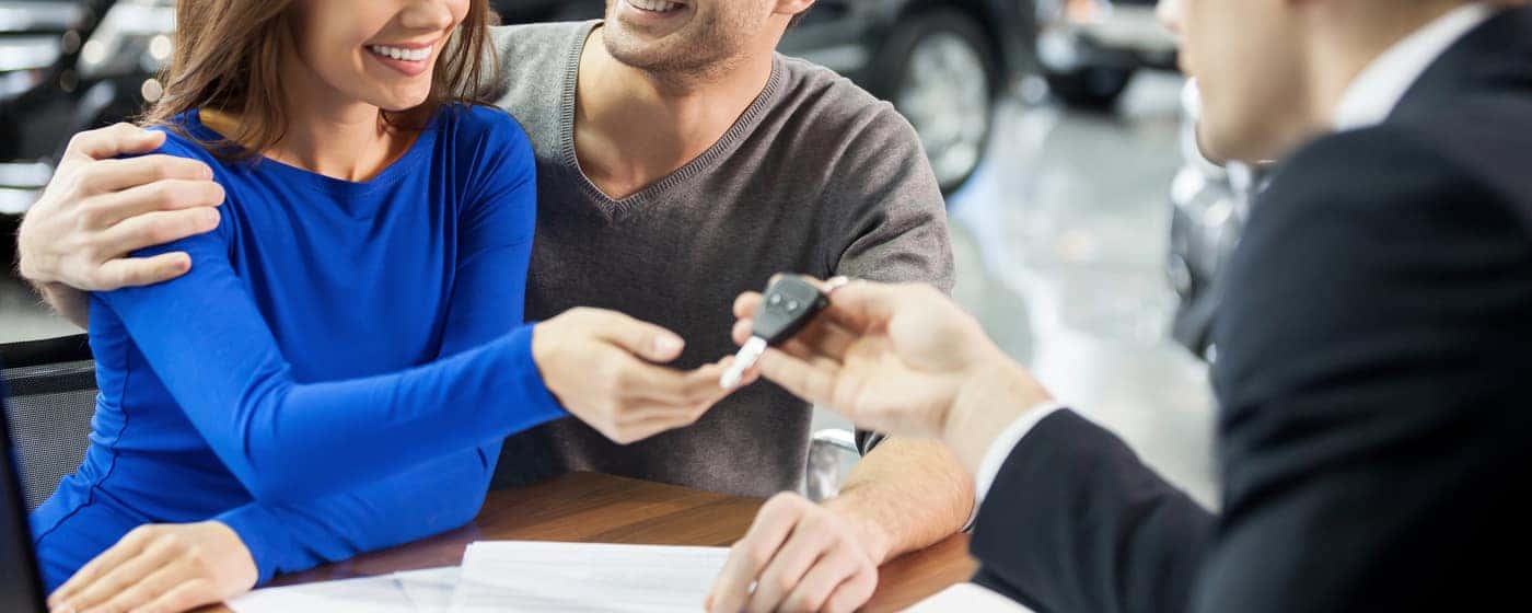 Now her dream comes true. Car salesman giving the key of the new car to the young attractive owners