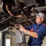 Car mechanic draining motor oil under lifted car at repair service station
