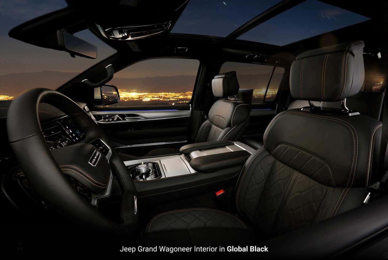 Interior view of the front cabin Jeep Grand Wagoneer in Global Black with a night city backdrop.