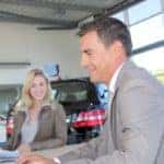 Car seller and couple of buyers signing contract