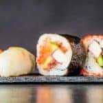 Row of sushi against black background and with reflection below