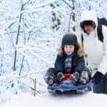 Young happy father and his cute laughing son sledding together in a snowy park
