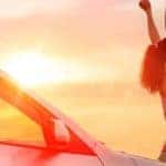 Woman raising arms in happiness at sunset with car