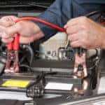 A car mechanic uses battery jumper cables to charge a dead battery