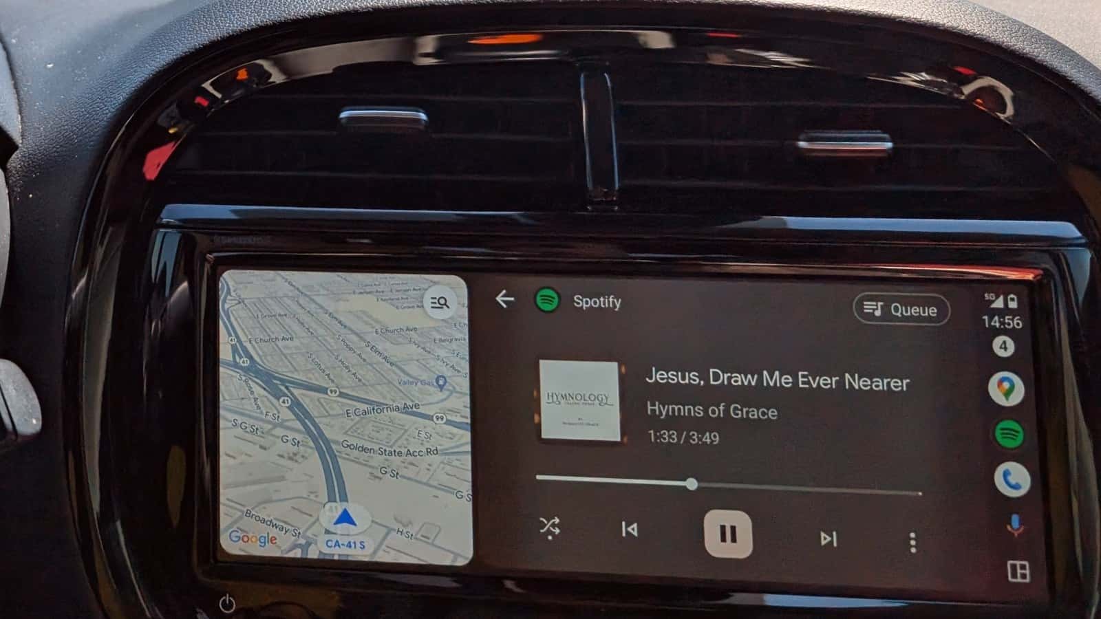 Android Auto showing a navigation map beside Spotify music controls on a car display, photographed in August 2024.