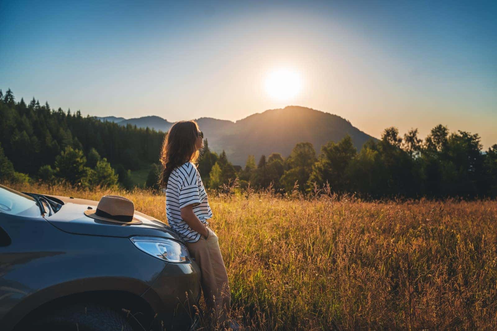 Woman standing beside a vehicle at sunset in a mountain field