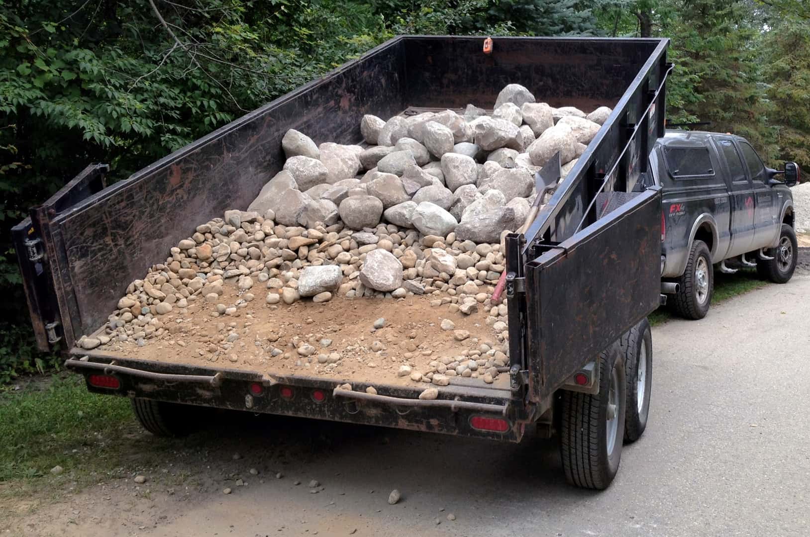 Pickup and a rock-filled dump trailer on a gravel driveway