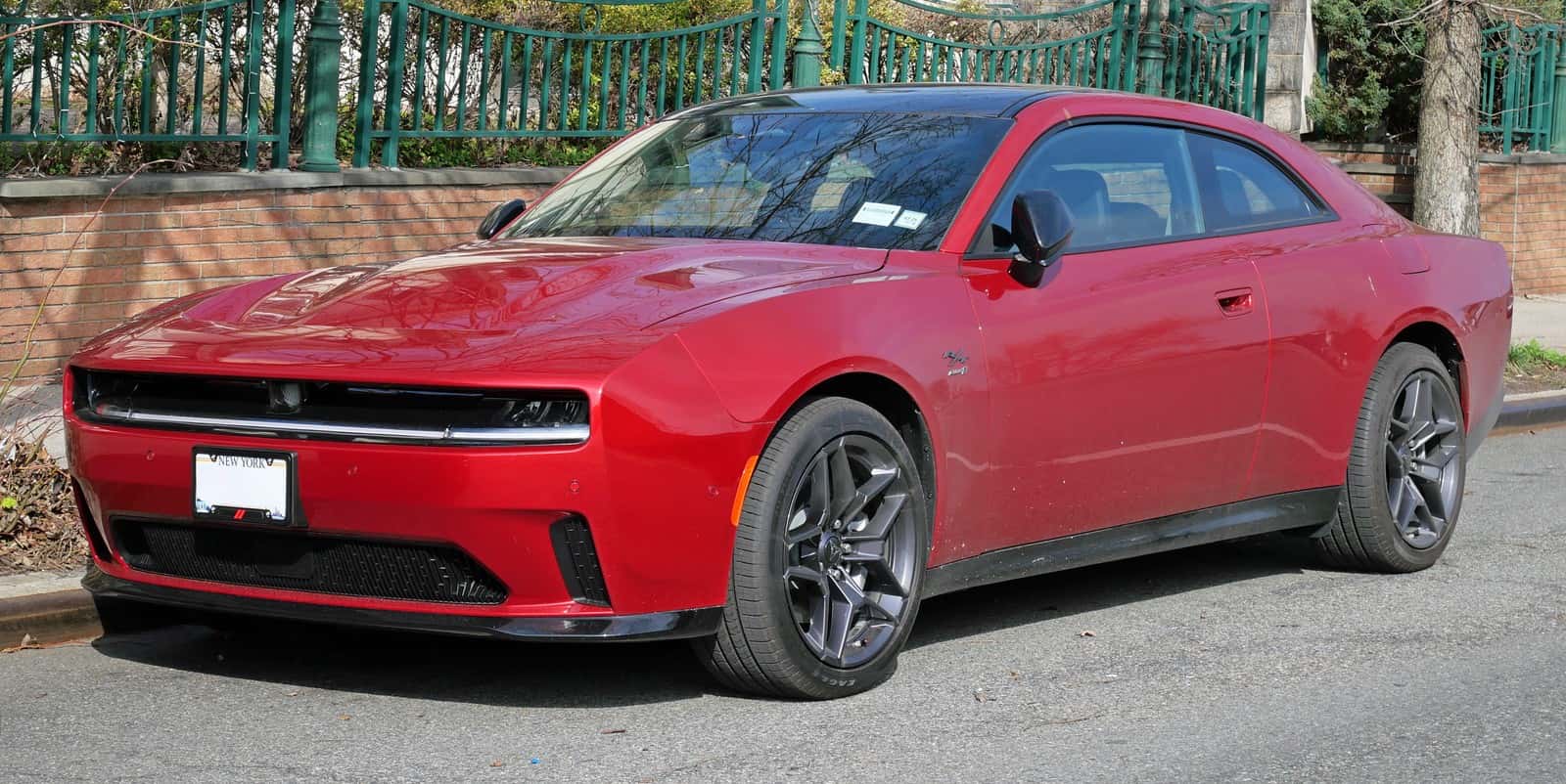 Red 2024 Dodge Charger Daytona R/T electric coupe parked beside a brick wall, viewed from the front left.