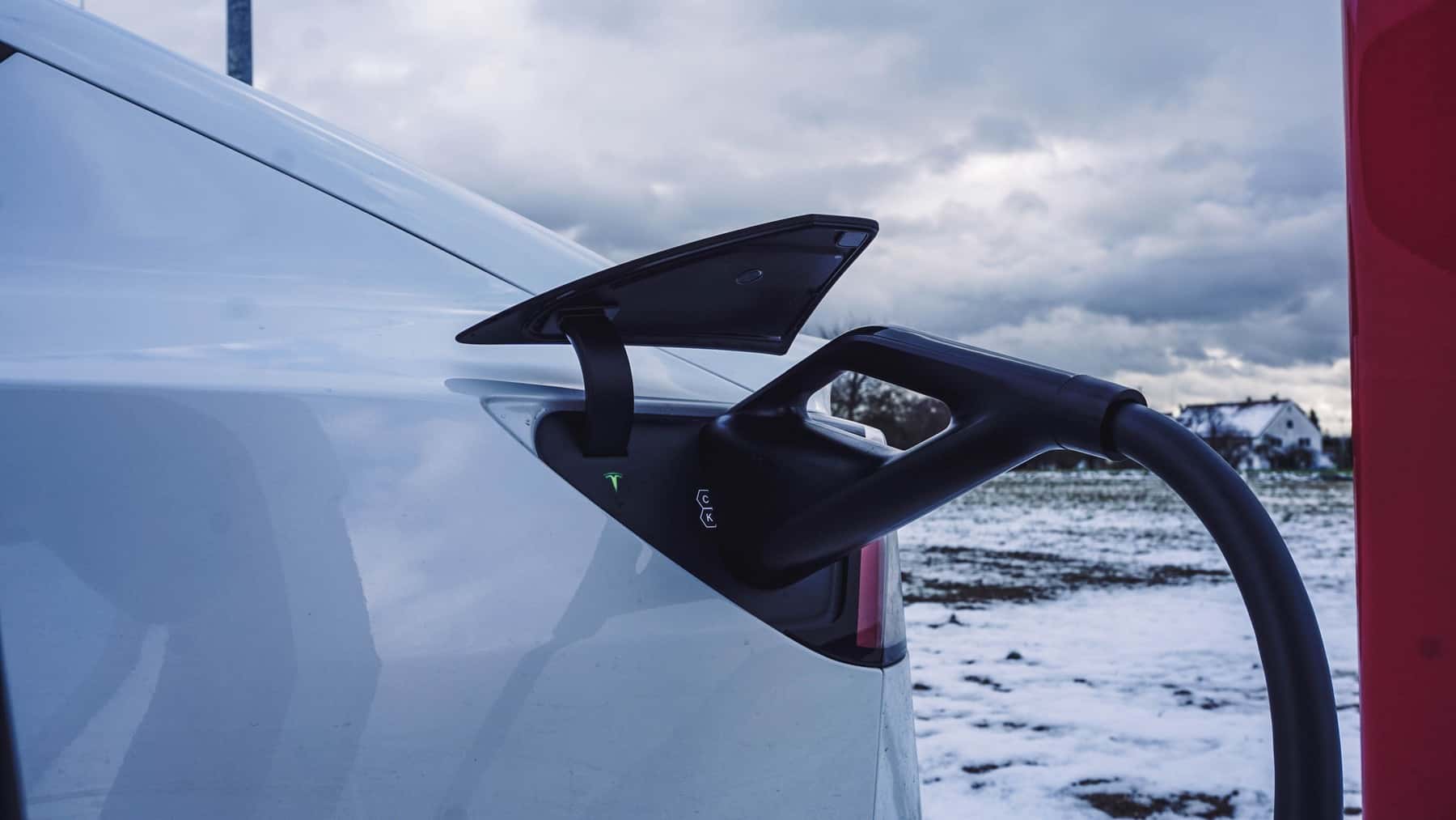 Charging connector plugged into a white Tesla with snow on the ground behind it