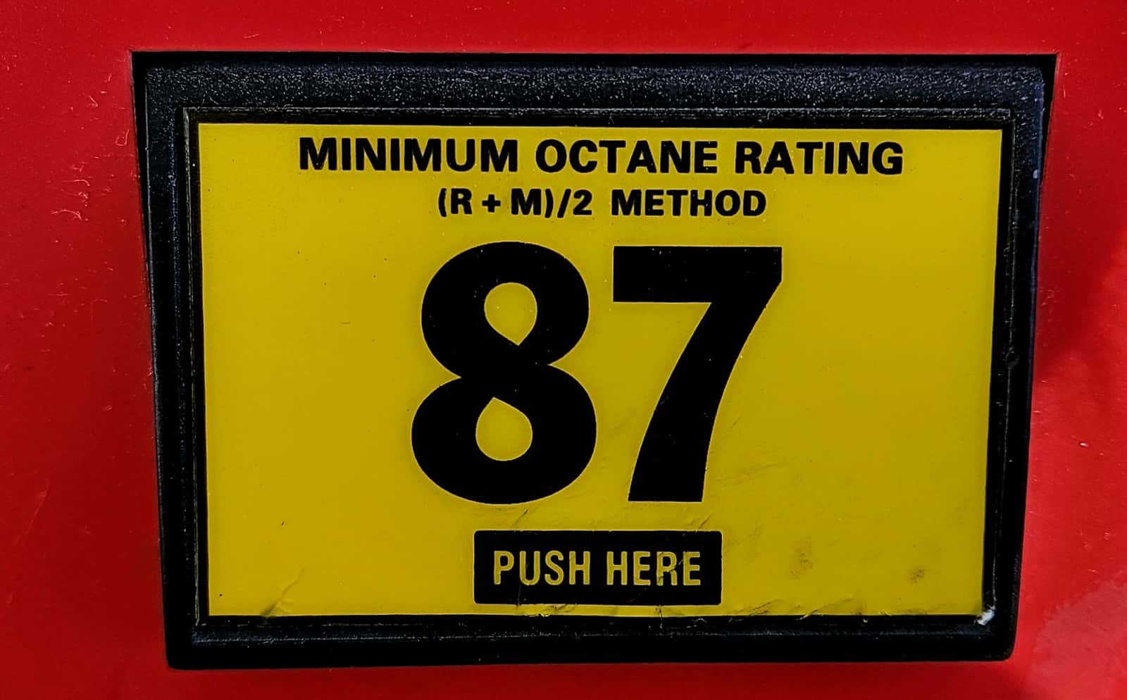 Close-up of a yellow gasoline pump selector labelled minimum octane rating 87 and (R + M)/2 method.
