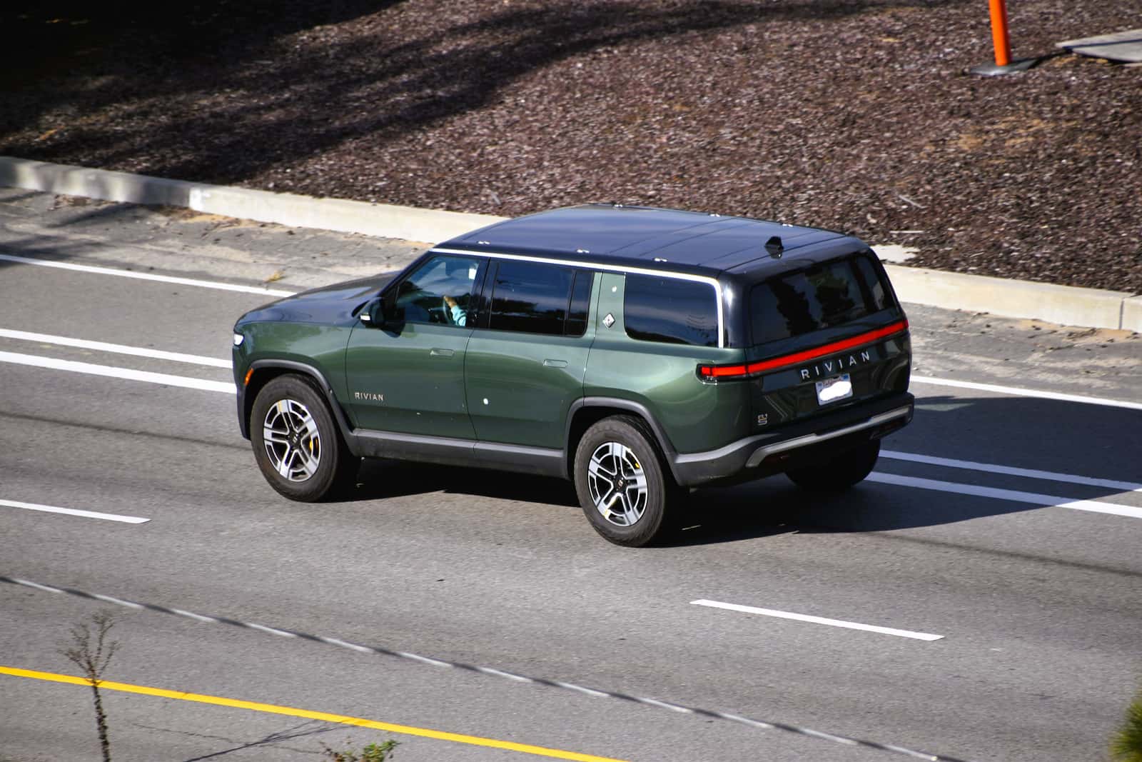 Green 2023 Rivian R1S seen from the rear three-quarter angle on a road
