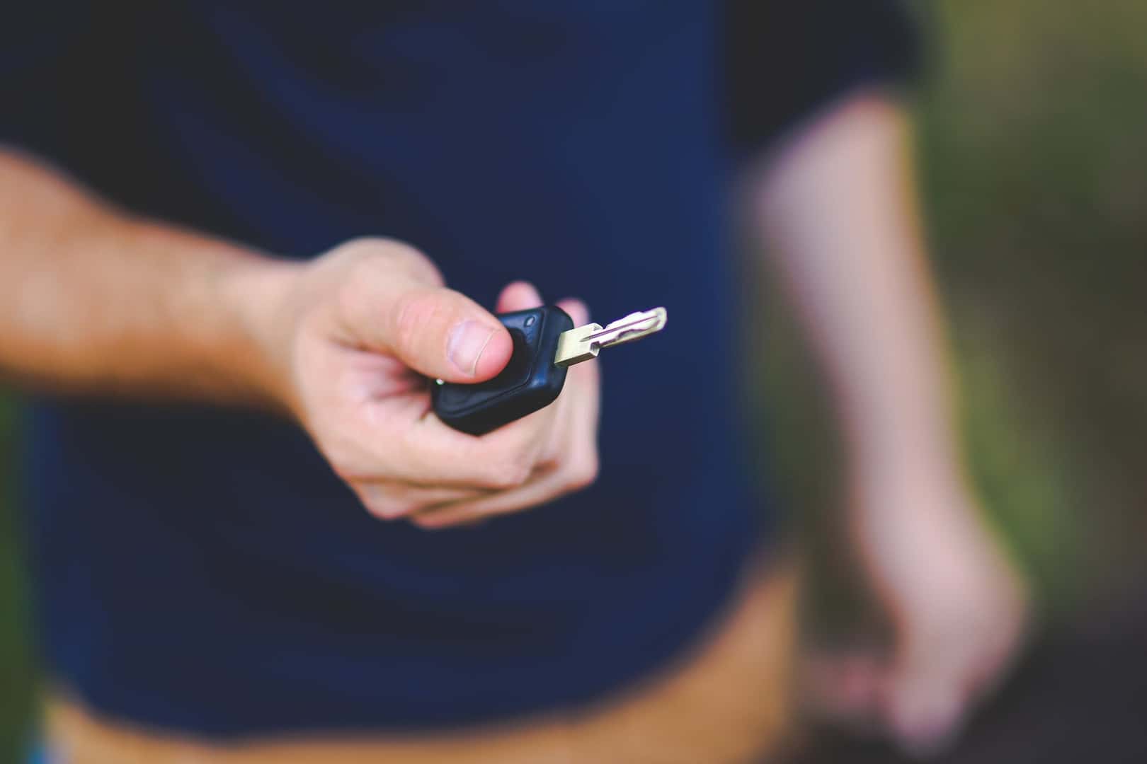 A person holding out a physical car key for handover.