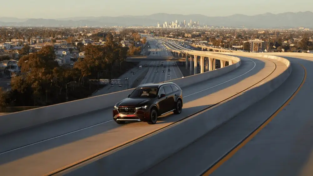 2026 Mazda CX-90 driving through city streets with sleek black exterior near Hempstead NY