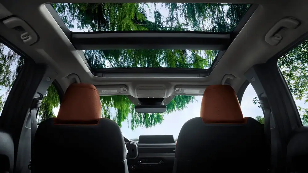 2026 Mazda CX-50 near Uniondale NY rear interior view showing dual-panel panoramic sunroof open to green tree canopy with tan front headrests visible
