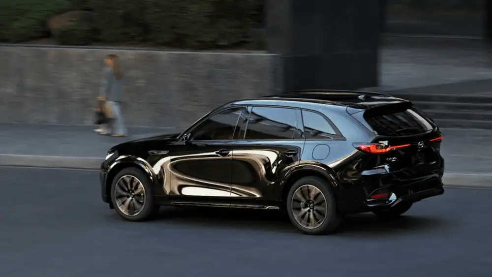 2026 Mazda CX-70 near Uniondale NY in jet black driving through urban street with motion-blurred background and pedestrian on sidewalk