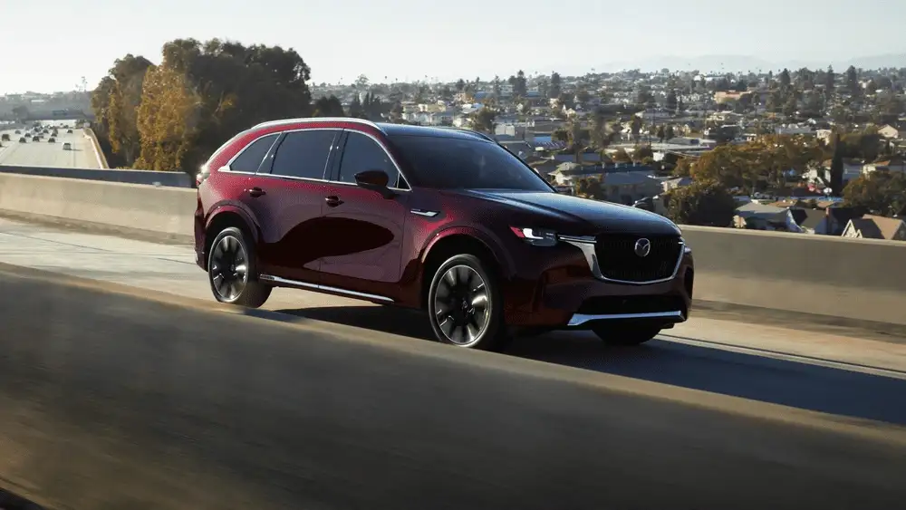 2026 Mazda CX-90 near Uniondale NY in deep red driving on elevated highway with city suburb skyline in background