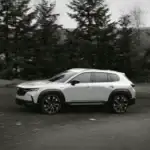 2026 Mazda CX-50 near Uniondale NY in white driving on open road surrounded by pine forest, ideal for outdoor lifestyle adventurers comparing it to the Toyota RAV4