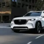 2026 Mazda CX-70 near Uniondale NY in jet black moving through a sunlit modern parking structure, highlighting quiet comfort for working professionals on long drives