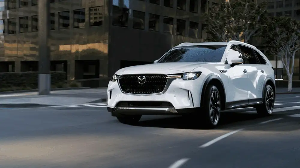 2026 Mazda CX-70 near Uniondale NY in jet black moving through a sunlit modern parking structure, highlighting quiet comfort for working professionals on long drives