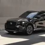 2026 Mazda CX-90 near Uniondale NY in white driving through city intersection at dusk, showcasing safety and confidence for family drivers