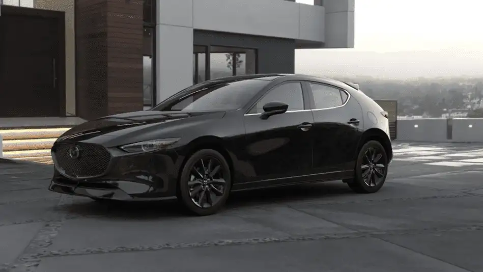2026 Mazda3 Hatchback out to Corona NY in Queens in jet black with black wheels parked on concrete lot in front of a modern wood and concrete building at dusk