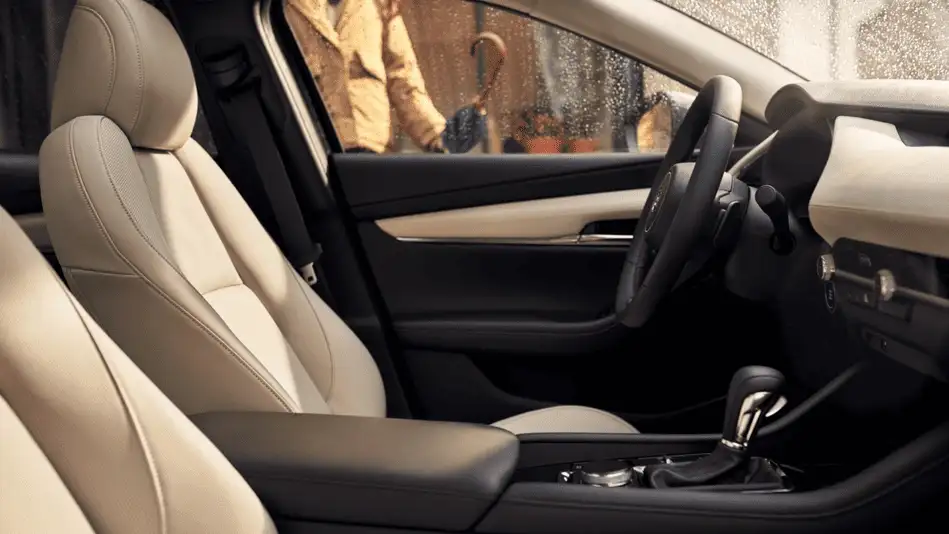 2026 Mazda3 Sedan out to Corona NY in Queens interior side view showing cream leather front seats and black steering wheel with rain-streaked window and pedestrian outside