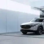 2026 Mazda CX-30 technology for Queens drivers shown in silver parked outside a modern minimalist home with large black entry door and glass facade