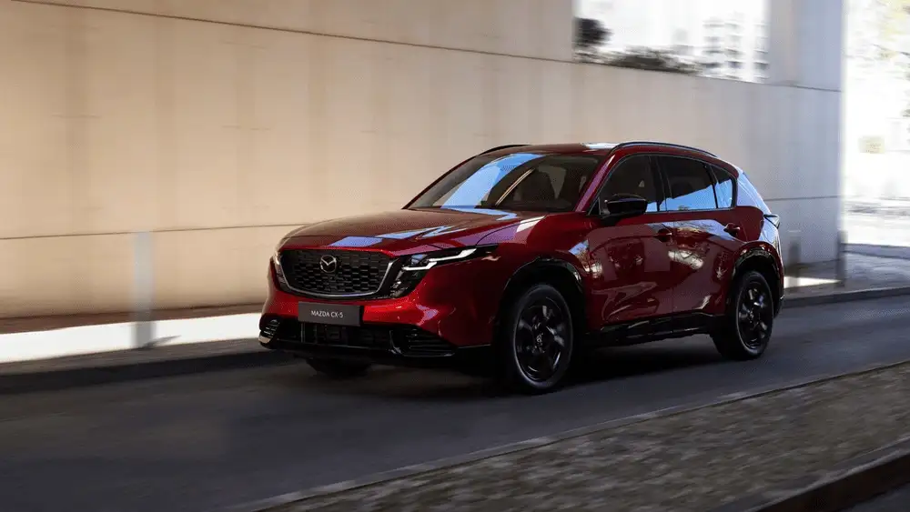 2026 Mazda CX-5 close to Uniondale NY in Soul Red Crystal with black wheels driving beneath an urban overpass in warm natural daylight