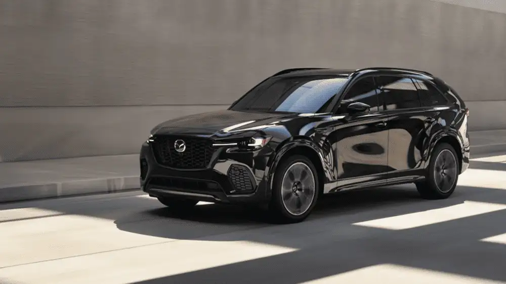 2026 Mazda CX-70 close to Uniondale NY in jet black moving through a sunlit modern parking structure with dramatic light and shadow across the pavement