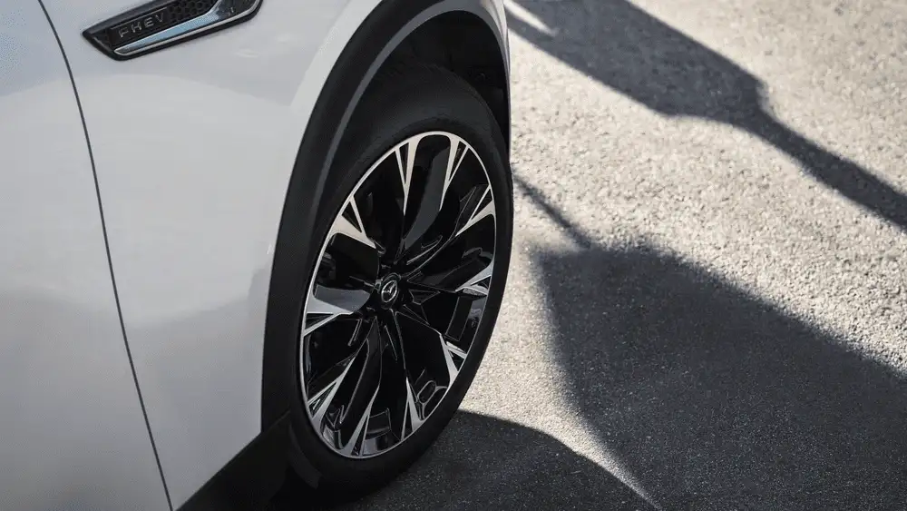 2026 Mazda CX-90 Plug-In Hybrid close to Uniondale NY close-up of multi-spoke black and silver alloy wheel with PHEV badge visible on white body panel