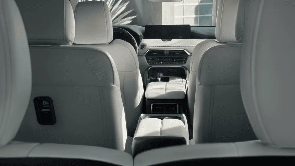 2026 Mazda CX-90 close to Uniondale NY in silver driving in profile past a classic brick theater facade with motion-blurred street in background
