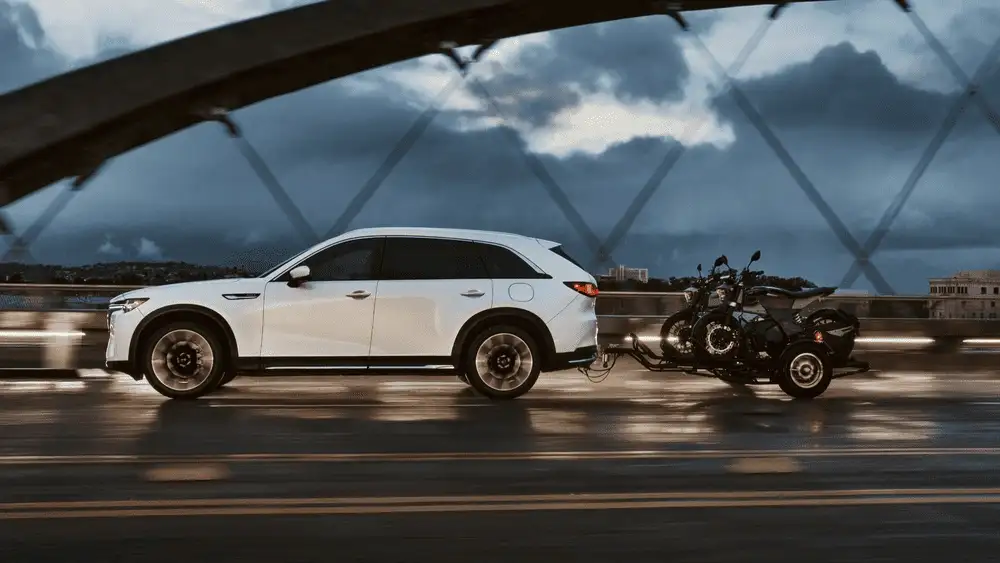 2026 Mazda CX-90 Plug-In Hybrid near Uniondale NY, white SUV towing a motorcycle trailer across a bridge