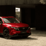 2026 Mazda CX-5 near Hempstead NY, red SUV with black wheels parked on gravel in front of a dark wood building