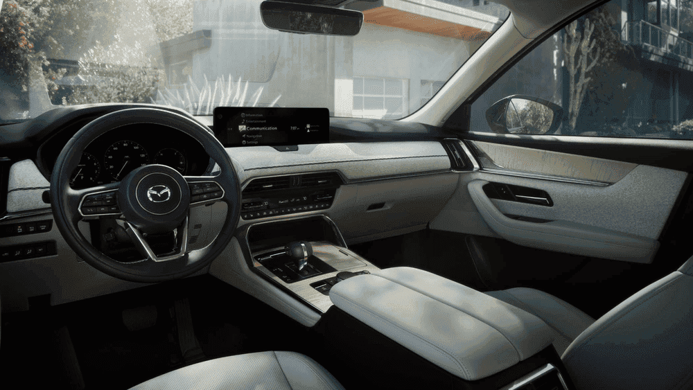 2026 Mazda CX-90 near Hempstead NY, light gray dashboard with Mazda steering wheel, wide infotainment screen, and sunlit suburban street through windshield