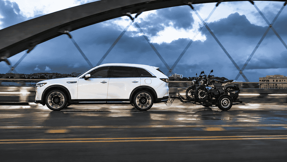 2026 Mazda CX-90 near Hempstead NY, white SUV towing a motorcycle trailer across a bridge at dusk