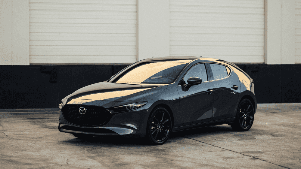 2026 Mazda3 Hatchback near Hempstead NY, dark gray hatchback with black wheels parked in front of a white industrial building
