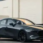 2026 Mazda3 Hatchback near Hempstead NY, dark gray hatchback with black wheels parked in front of a white industrial building