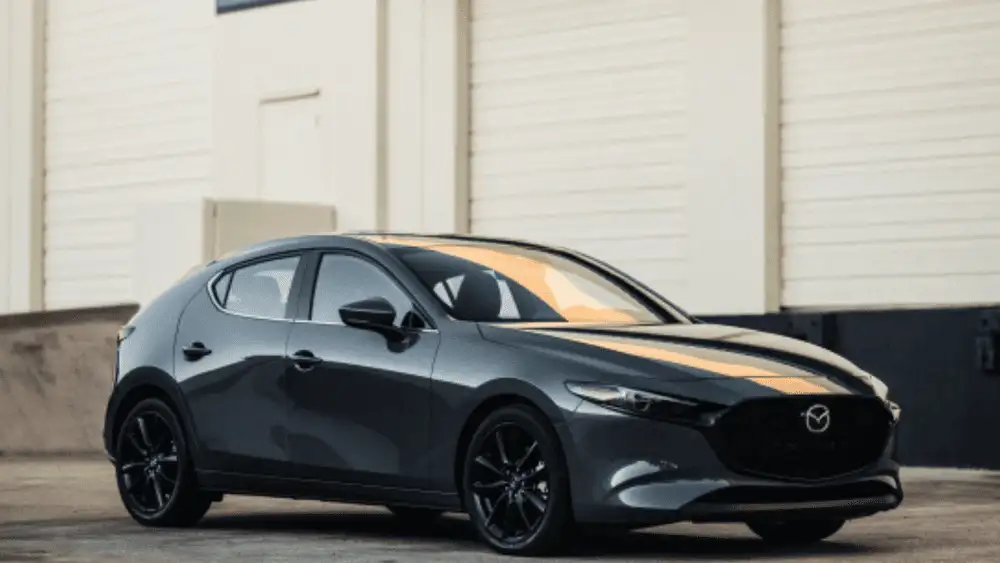 2026 Mazda3 Hatchback near Hempstead NY, dark gray hatchback with black wheels parked in front of a white industrial building