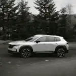 2026 Mazda CX-50 Hybrid near Hempstead NY, white SUV driving in profile on an open road surrounded by pine trees
