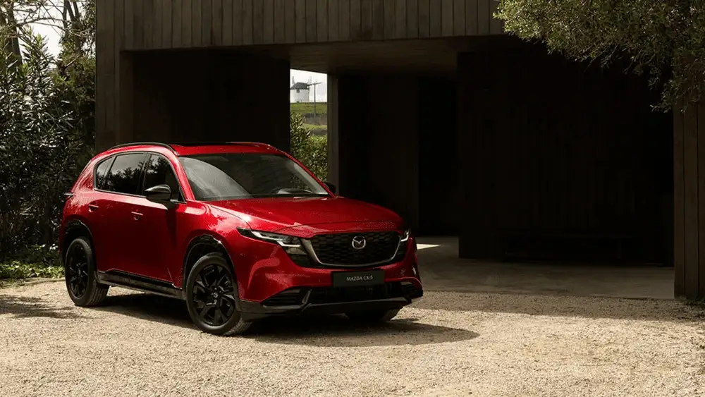 2026 Mazda CX-5 in red parked outside a modern building near Uniondale, NY, vs. Honda CR-V.