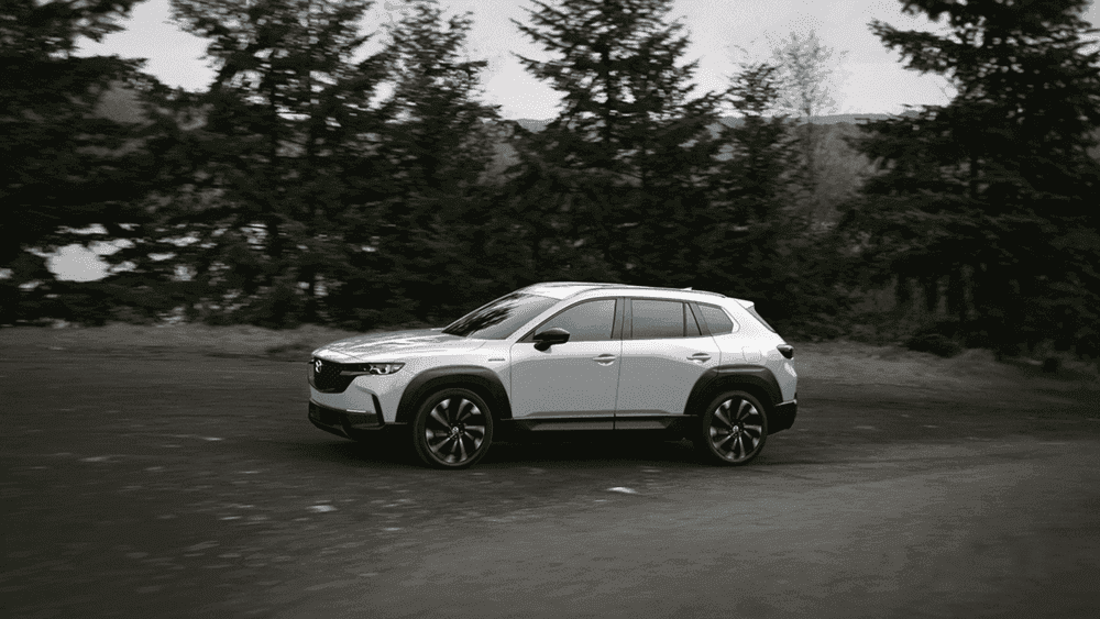 2026 Mazda CX-50 Hybrid in white driving through a forest road near Uniondale, NY.