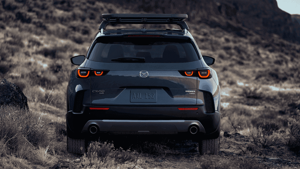 2026 Mazda CX-50 rear view in gray with roof rack on rugged terrain near Uniondale, NY.
