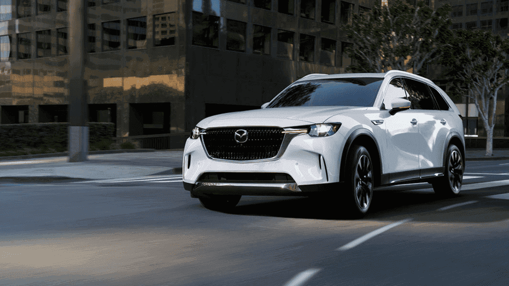 2026 Mazda CX-90 Plug-In Hybrid in white driving through city street near Uniondale, NY.