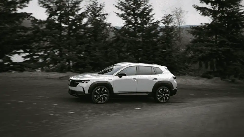 2026 Mazda CX-50 Hybrid in white driving through a forest road near Uniondale, NY.