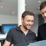Salesman going over papers with customer in front of a car