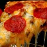 Slice of pepperoni pizza being removed from whole pizza with tomatoes in background.