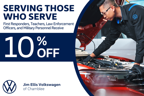 Volkswagen technician working under the hood of a red vehicle in a service bay. Graphic states first responders, teachers, law enforcement officers, and military personnel receive 10 percent off service at Jim Ellis Volkswagen of Chamblee.