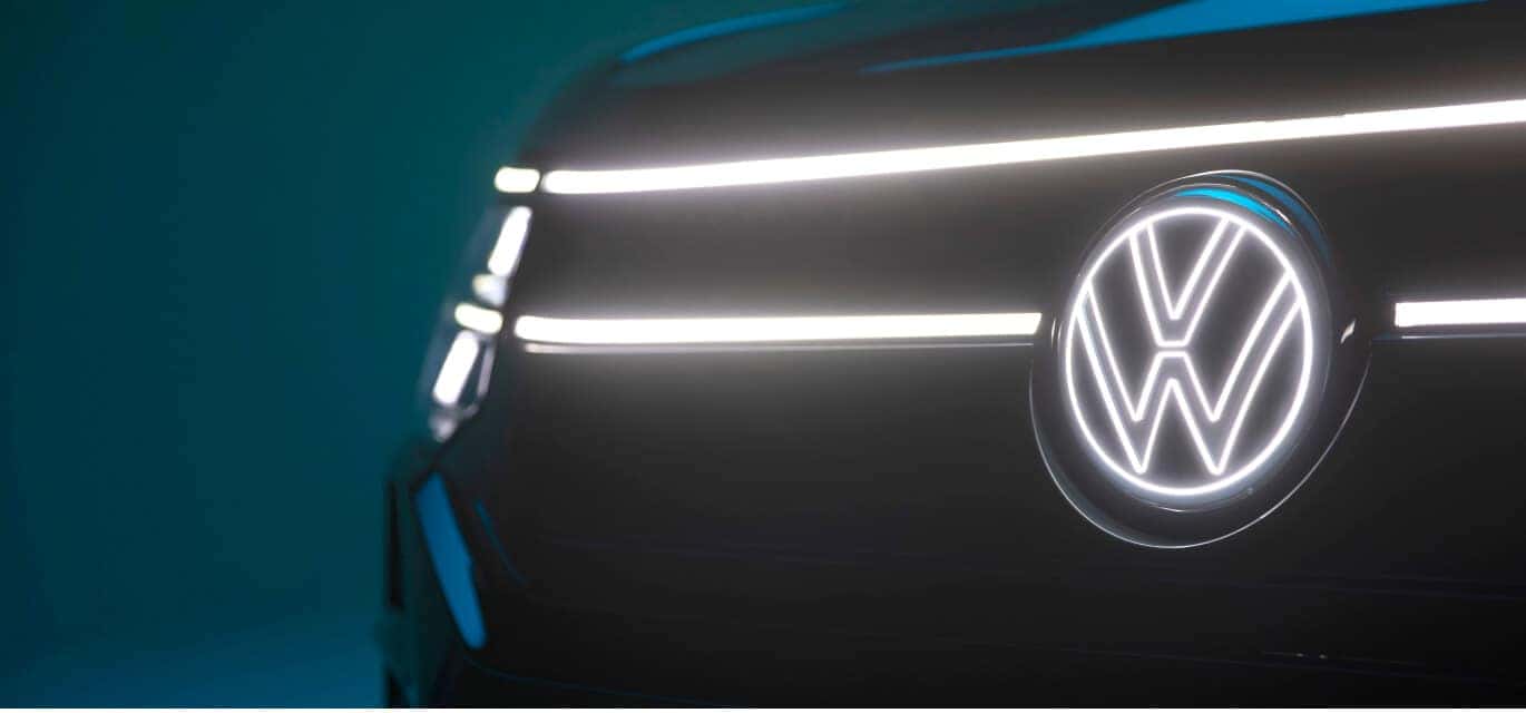 Close-up of a Sacramento Green 2027 Volkswagen Atlas SEL Premium R-Line showing its illuminated LED front grille and logo.
